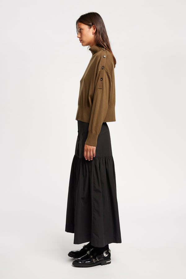 Side view of Model wearing merino wool mock neck sweater with shoulder button detail in brown.
