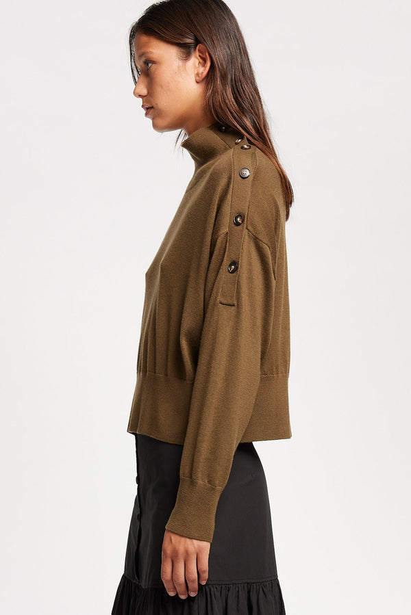 Side view of Model wearing merino wool mock neck sweater with shoulder button detail in brown.