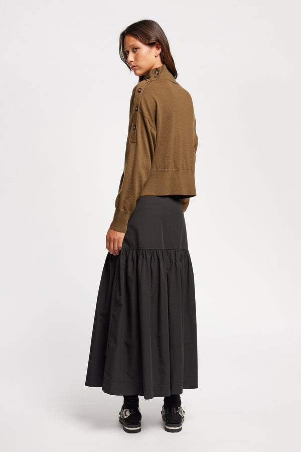 Back angle view of Model wearing merino wool mock neck sweater with shoulder button detail in brown.