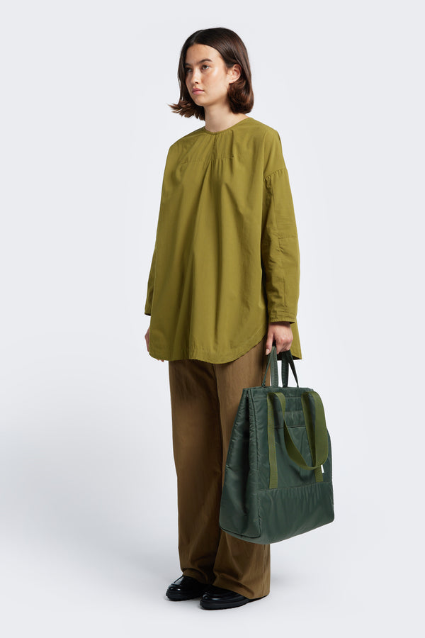 Model holding the Influx Padded Bag Olive, a practical tote with four compartments, including two snap-closing pockets.
