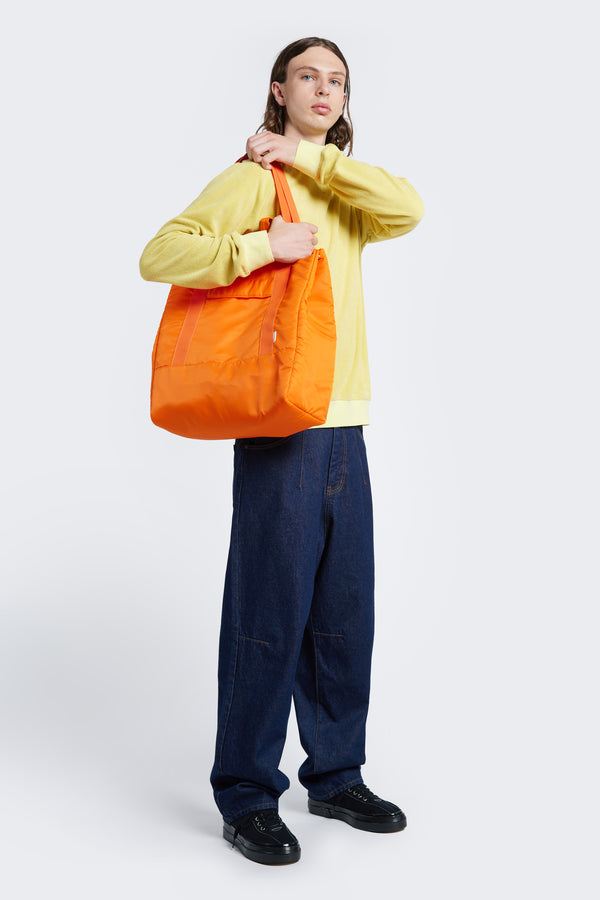 Model carries the Influx Padded Bag Orange over his shoulder. This practical tote bag has a padded look and feel, four compartments and is made from a strong, quick dry nylon.