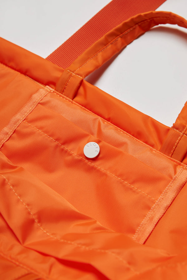 The Influx Padded Bag Orange has a snap lock pocket on the inside. This practical tote bag has two strap lengths.