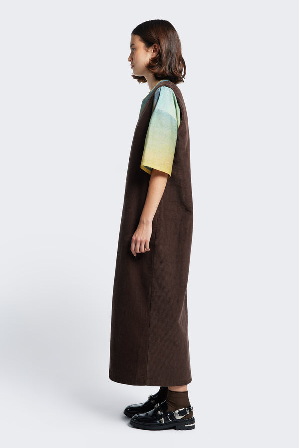 Side view of the Arc Dress, a full-length pinafore dress made from thick-wale corduroy in Dark Brown.