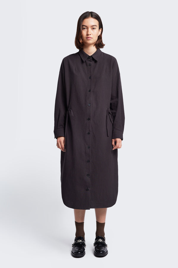 The Filter Dress Black, a classic style with a button through partly concealed placket, collar, rounded scoop hemline and long sleeves. Featuring waist ties to adjust the waistline to your liking.