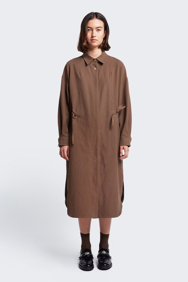 The Filter Dress Brown, a classic style with a button through partly concealed placket, built in collar, rounded scoop hemline, in seam side pockets and long sleeves. Featuring waist ties to adjust the waistline to your liking.