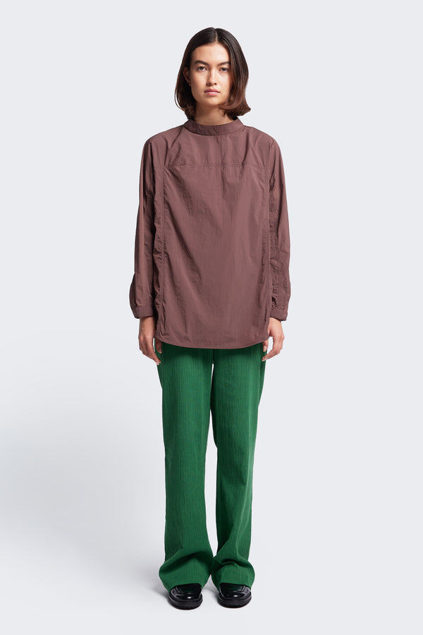 The Women's Waking Blouse Cocoa Brown is a relaxed, long sleeve shirt made from 100% nylon. Featuring panel stitch detail, a stand collar with centre back button opening, dropped shoulders and a hem cuff with button opening.