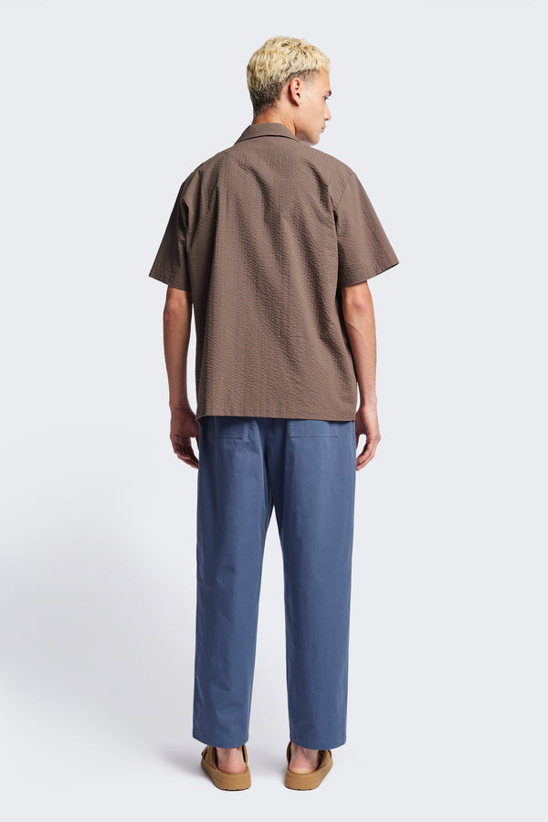 Back of The Boulder Pleat Pants in Blue, crafted from cotton herringbone twill, featuring side slant pockets, back patch pockets, and an elastic waistband with internal pull. Available in 5 sizes.