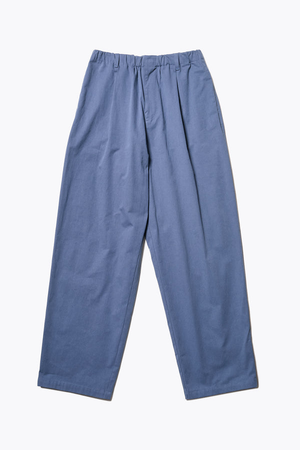 The Boulder Pleat Pants in Blue, crafted from cotton herringbone twill, featuring side slant pockets, back patch pockets, and an elastic waistband with internal pull. Available in 5 sizes.