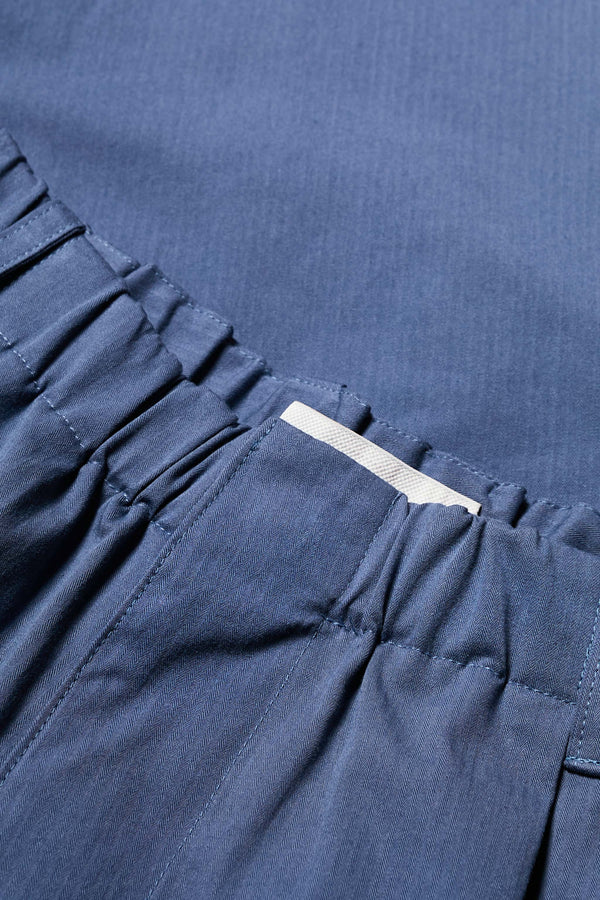 Close up details of The Boulder Pleat Pants in Blue, crafted from cotton herringbone twill, featuring side slant pockets, back patch pockets, and an elastic waistband with internal pull. Available in 5 sizes.