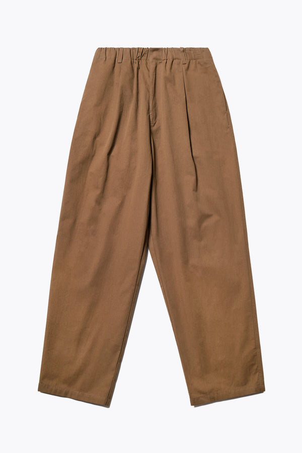 The Boulder Pleat Pants in Brown, crafted from cotton herringbone twill, featuring side slant pockets, back patch pockets, and an elastic waistband with internal pull. Available in 5 sizes.