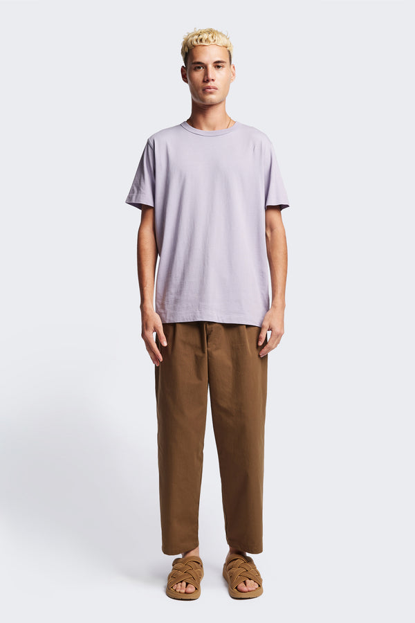 The Boulder Pleat Pants in Brown, crafted from cotton herringbone twill, featuring side slant pockets, back patch pockets, and an elastic waistband with internal pull. Available in 5 sizes.