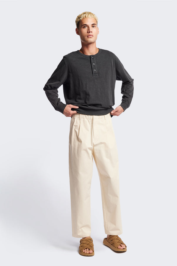 The Boulder Pleat Pants in Chalk Beige, crafted from cotton herringbone twill, featuring side slant pockets, back patch pockets, and an elastic waistband with internal pull. Available in 5 sizes.