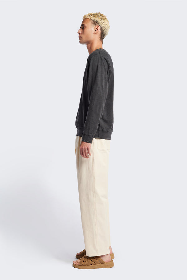 Side of The Boulder Pleat Pants in Chalk Beige, crafted from cotton herringbone twill, featuring side slant pockets, back patch pockets, and an elastic waistband with internal pull. Available in 5 sizes.