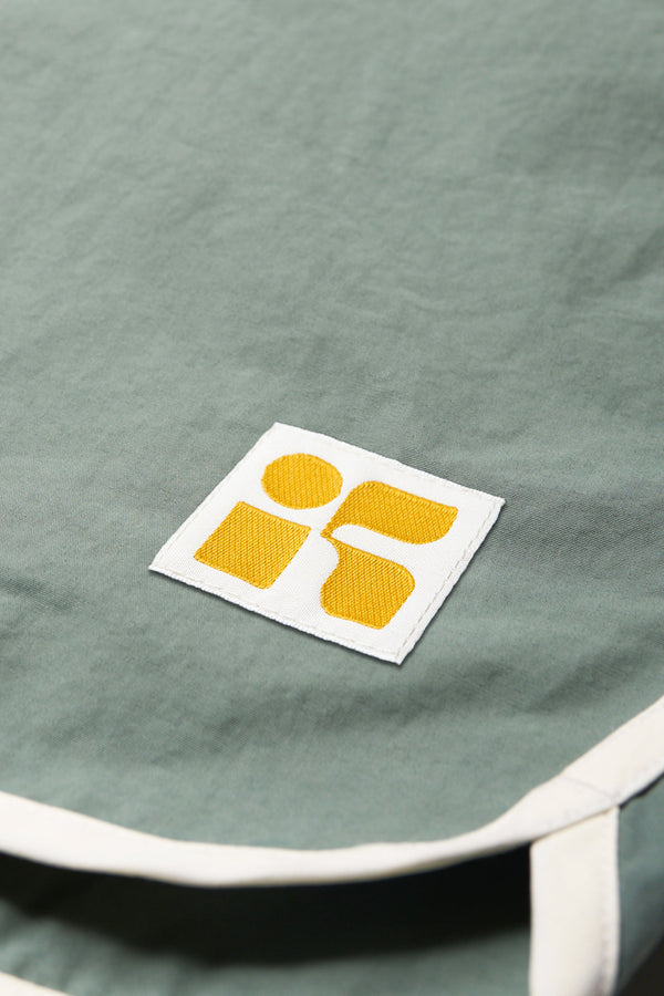 Close up details shot of The Hybrid Board short in Sage Green, made from a functional technical cotton/nylon thats durable, stashable and quick-drying. Featuring back patch pocket with Velcro closure. Available in 5 sizes.