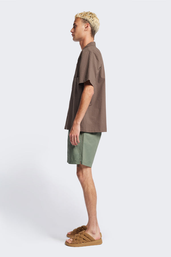 Side of The Mirari Shirt in Brown, a relaxed short-sleeve camp shirt in soft textured cotton seersucker with an open collar and laid-back fit, styled for versatile wear. Available in 5 sizes.