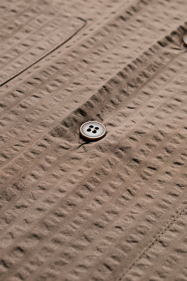 Close up fabric shot of The Mirari Shirt in Brown, a relaxed short-sleeve camp shirt in soft textured cotton seersucker with an open collar and laid-back fit, styled for versatile wear. Available in 5 sizes.