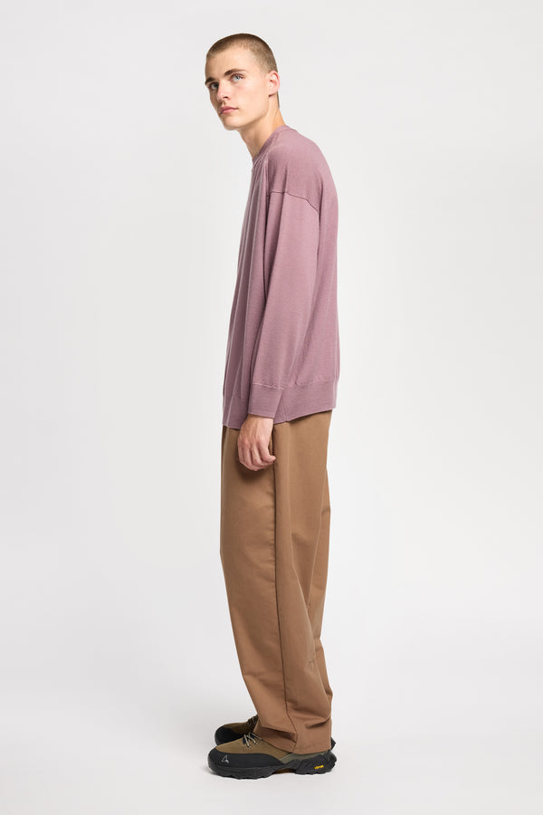 Side of Model wearing loose fit merino wool crew neck sweater with exposed seams in mauve.