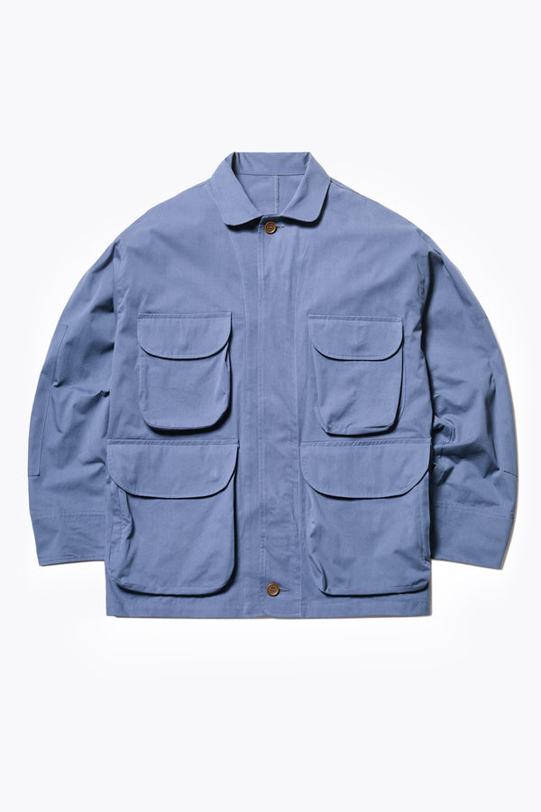 The Pressure Jacket in Blue, a relaxed boxy long sleeve jacket in washed cotton herringbone with 3D patch pockets and hidden zip openings. Available in 5 sizes.