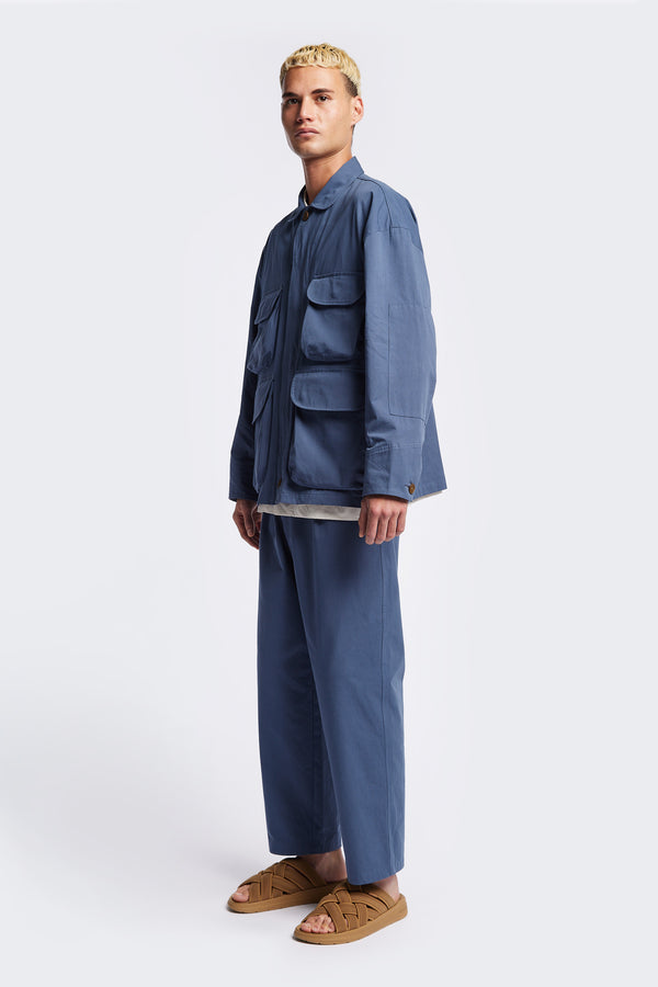 The Pressure Jacket in Blue, a relaxed boxy long sleeve jacket in washed cotton herringbone with 3D patch pockets and hidden zip openings. Available in 5 sizes.