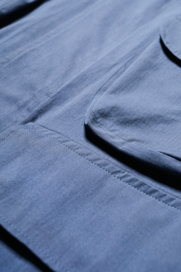 Close up details on The Pressure Jacket in Blue, a relaxed boxy long sleeve jacket in washed cotton herringbone with 3D patch pockets and hidden zip openings. Available in 5 sizes.