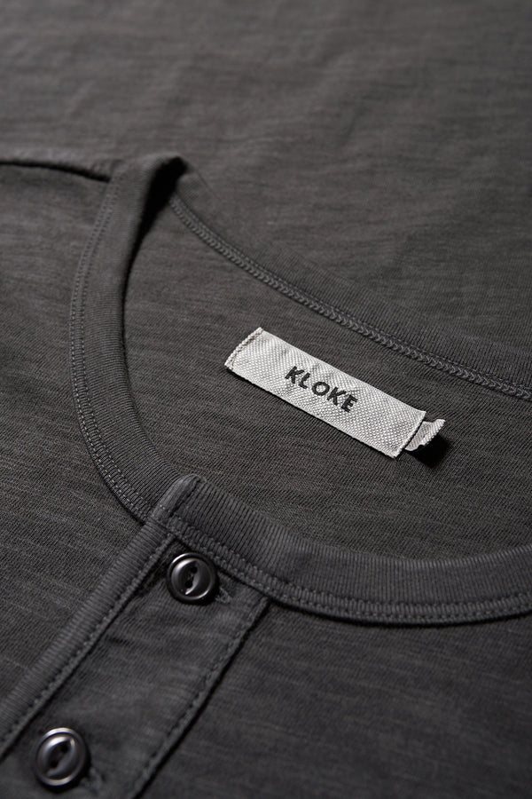 Close up details of The Stratus Henley T-shirt in Vintage Black. Garment-dyed in soft cotton jersey with three-button placket and coverstitched hems. Available in 5 sizes.