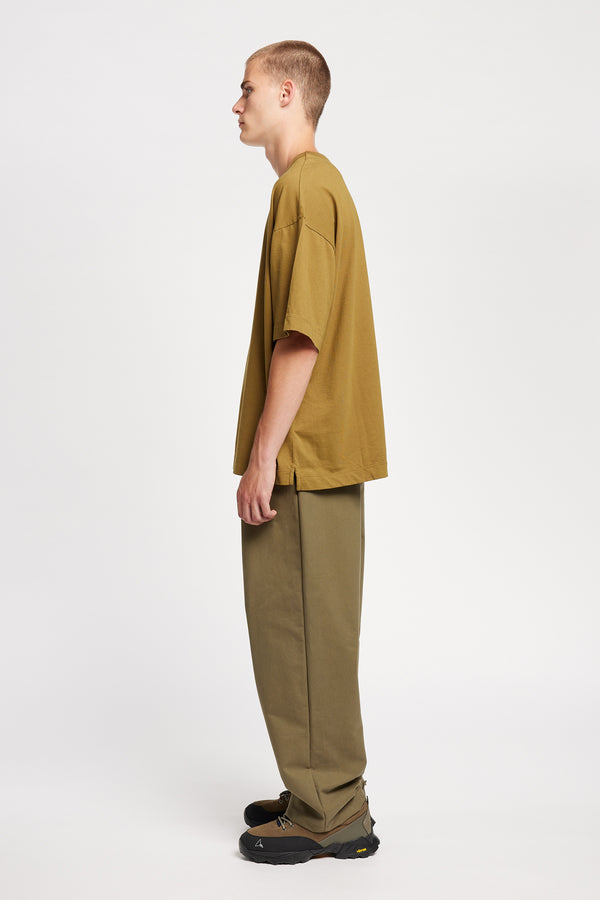 Side of male model in Monolith Unisex Tee in Olive Oil. Oversized relaxed fit. Available in 6 sizes.