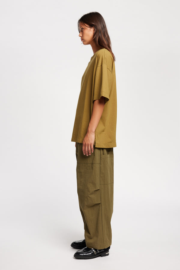 Side of female model in the Monolith Unisex Tee in Olive Oil. Oversized relaxed fit. Available in 6 sizes. Made from 100% Organic Cotton.