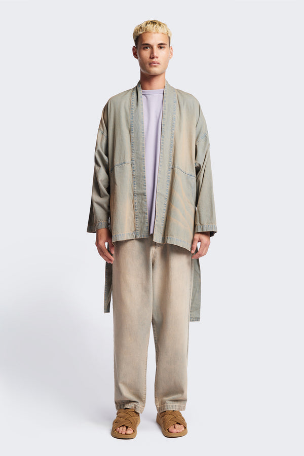 Front of the unisex Subterra Wide wrap shawl collar jacket with kimono-style sleeves, crafted from cotton denim, featuring front patch pockets and a waist tie to cinch the loose silhouette. Available in 5 sizes.