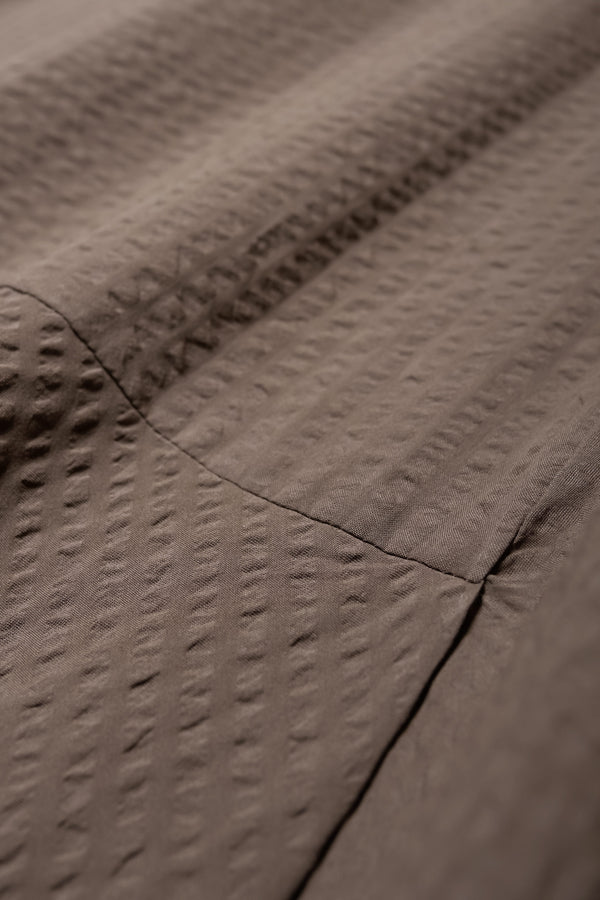 Close up shot of the Abroad Panel Skirt, fitted at the waist with a bias-cut maxi silhouette, made from 100% cotton in Brown Seersucker. Features panel details, side pockets, and an invisible back zip. Available in 6 sizes