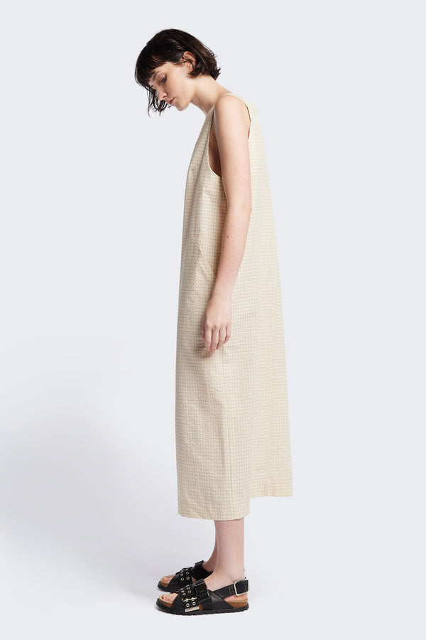 Side view of Long-length Forces Pinafore Dress in Ecru Beige Kloke designed soft seersucker premium cotton . Relaxed fit with a deep rounded neckline, front patch pockets, and a front split for ease of movement. Available in 5 sizes.