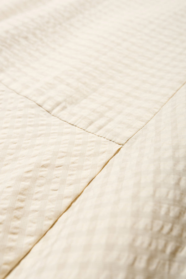 Close up fabric shot of the Long-length Forces Pinafore Dress in Ecru Beige Kloke designed soft seersucker premium cotton. Relaxed fit with a deep rounded neckline, front patch pockets, and a front split for ease of movement. Available in 5 sizes.