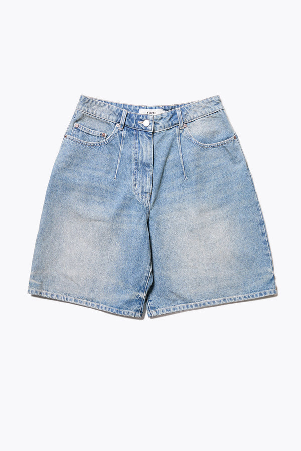 The Fuego Longline denim shorts in a blue fade with a subtle pink tint, featuring darted waist details and a relaxed wide-leg design. Available in 6 sizes.