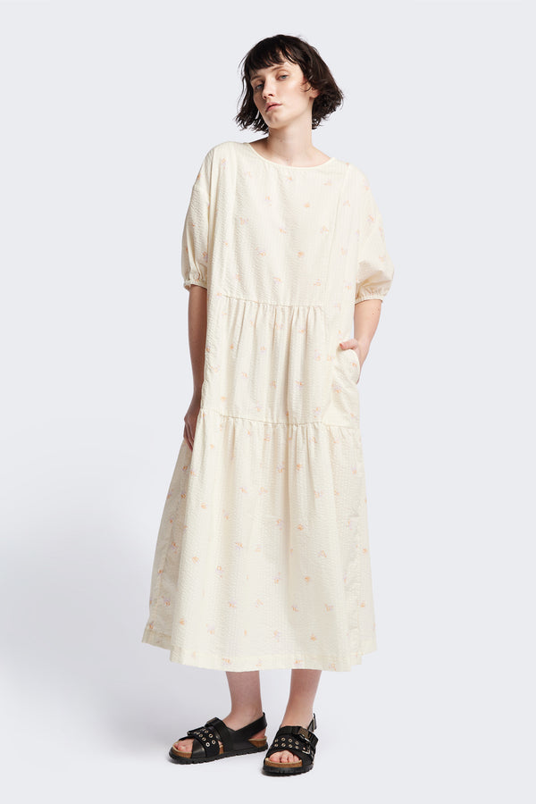 Front of the Gradient Dress in Ecru, a panelled dropped sleeve dress in Kloke's floral seersucker print, featuring a tiered gathered skirt, in-seam pockets, and elastic cuff sleeves.