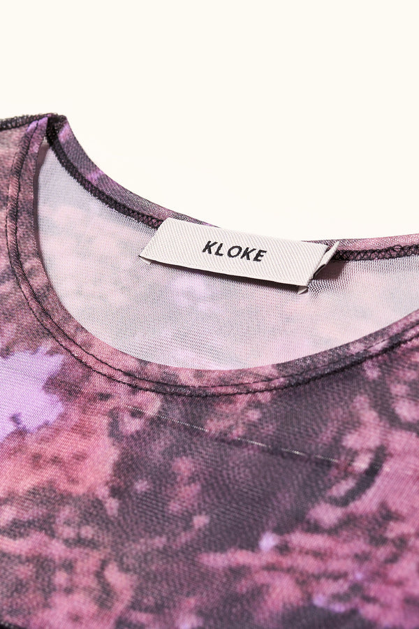 Close up fabric detail shot of the Inlet Top in Real Tree purple print, featuring a slim fit, semi-sheer mesh fabric, and black baby lock stitching.