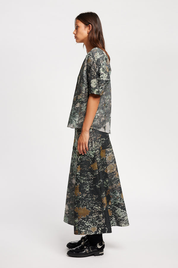 Side view model in the Optic Skirt a midi-length A-line skirt in textured jacquard green print fabric with a forest-inspired pattern, designed by Kloke