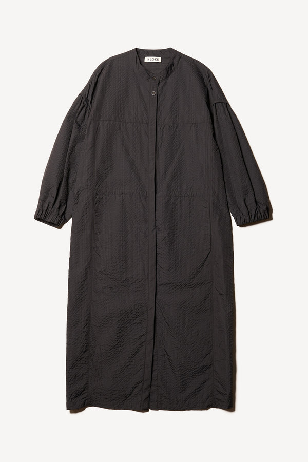 Flat front of the Parapet Dress in Jet Black A lightweight seersucker nylon, showing band collar and adjustable front waist tie.