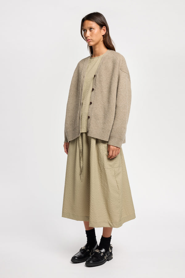 Front angle view of model wearing oversized ribbed wool cardigan with button closure in light taupe