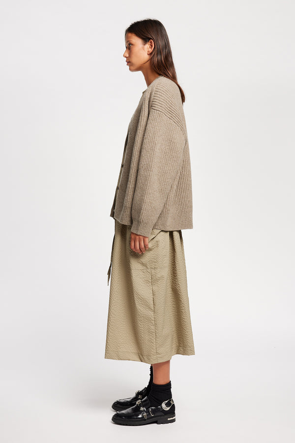 Side view of model wearing oversized ribbed wool cardigan with button closure in light taupe