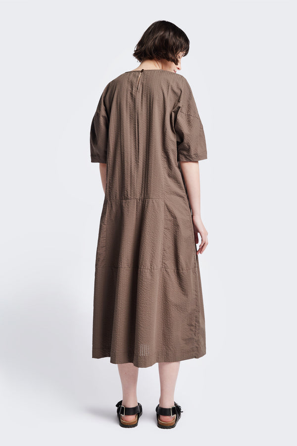 Back of the Scoria Dress in brown, a long-panelled cotton seersucker dress with voluminous sleeves, structured panel details, and a fuller skirt, perfect for an effortless summer look. Available in 5 sizes.