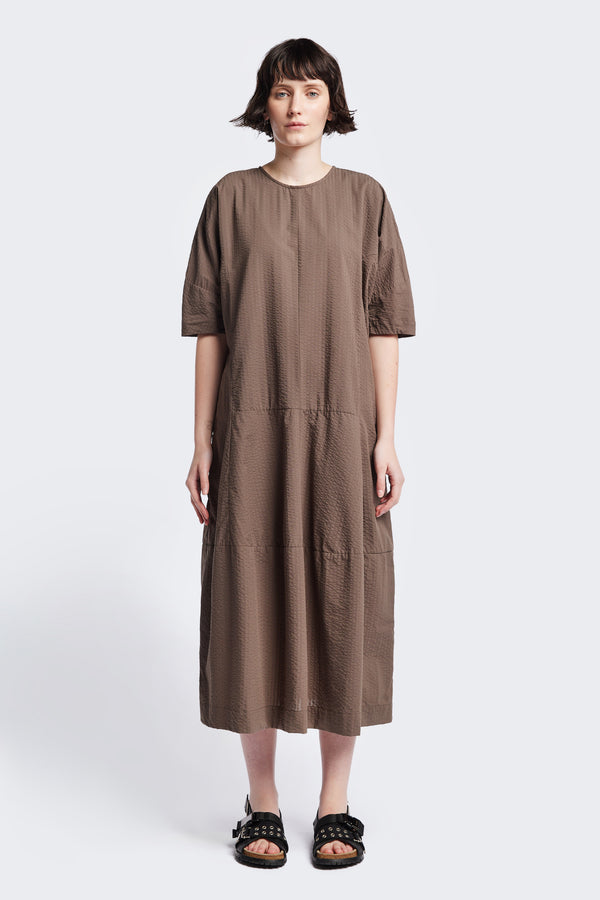 The Scoria Dress, in brown, a long-panelled cotton seersucker dress with voluminous sleeves, structured panel details, and a fuller skirt, perfect for an effortless summer look. Available in 5 sizes.