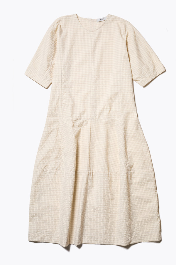 The Scoria Dress in Ecru beige, a long-panelled cotton seersucker dress with voluminous sleeves, structured panel details, and a fuller skirt, perfect for an effortless summer look. Available in 5 sizes.