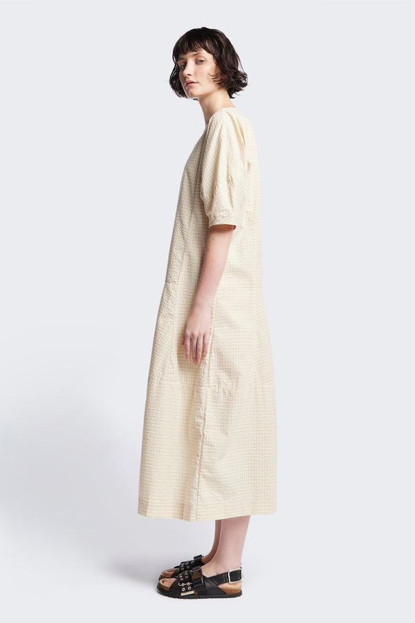 Side of the Scoria Dress in Ecru beige, a long-panelled cotton seersucker dress with voluminous sleeves, structured panel details, and a fuller skirt, perfect for an effortless summer look. Available in 5 sizes.