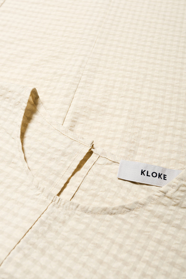 Close up fabric shot of the Scoria Dress in Ecru beige, a long-panelled cotton seersucker dress with voluminous sleeves, structured panel details, and a fuller skirt, perfect for an effortless summer look. Available in 5 sizes.