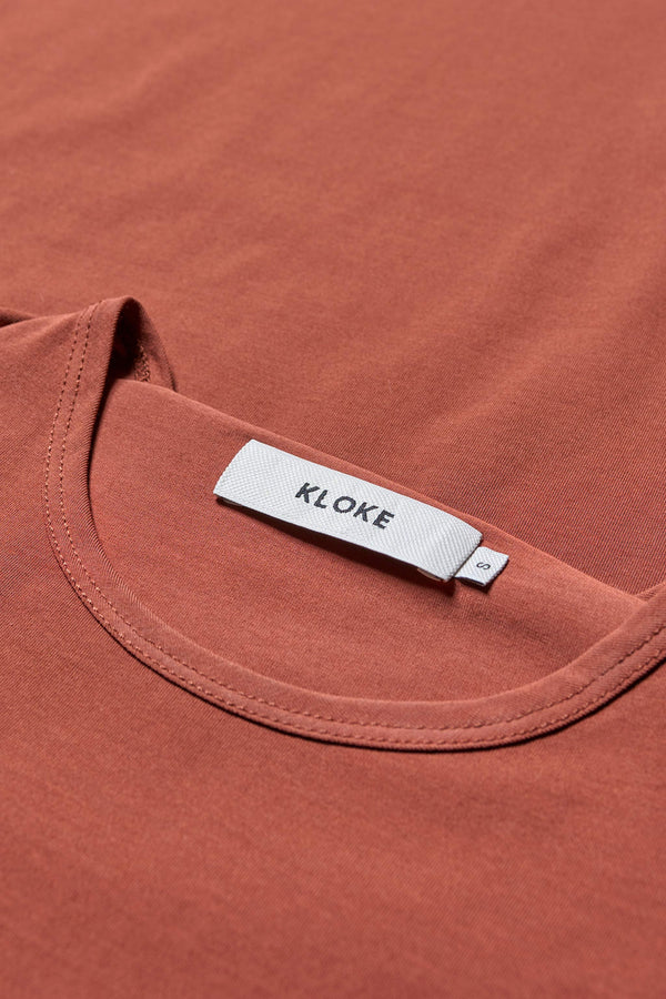 Close up fabric details of the Seclude long sleeve top in Brick. A Slim-fit crew neck top in soft cotton stretch, featuring an exposed bound seam curving across the back and sleeves.