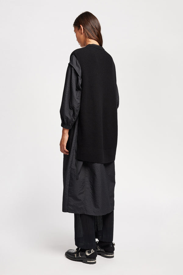 Back Angle view of model wearing the black sleeveless ribbed knit vest with side ties in merino and cotton blend