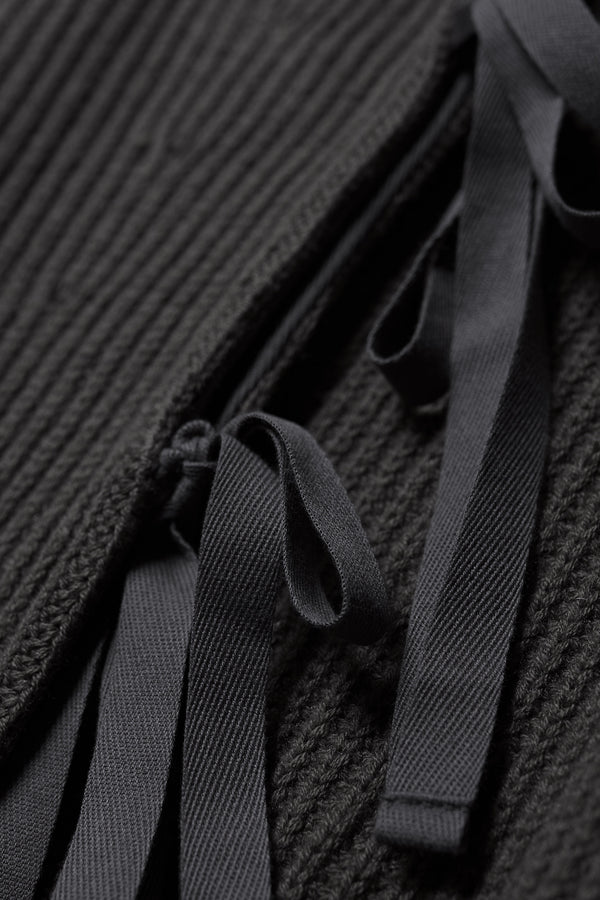 Close up fabric detail shot of black
sleeveless ribbed knit vest with side ties in merino and cotton blend