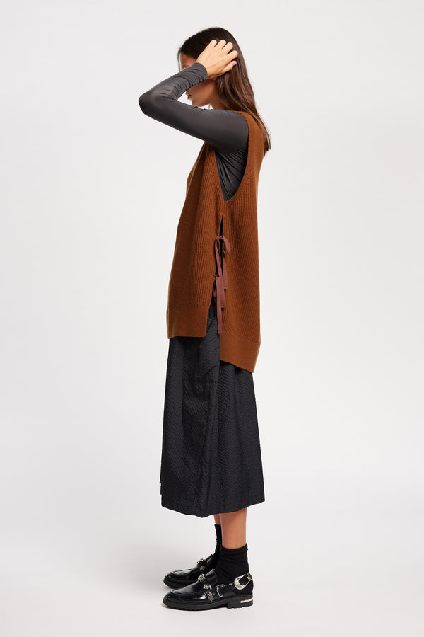 Side view of model wearing toffee brown sleeveless ribbed knit vest with side ties in merino and cotton blend