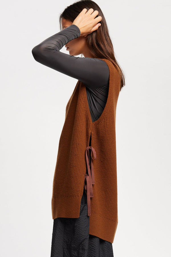 Side view of model wearing toffee brown sleeveless ribbed knit vest with side ties in merino and cotton blend