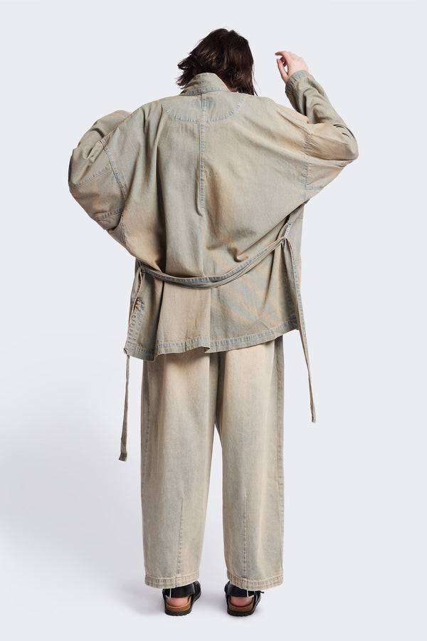 Back of the unisex Subterra Wide wrap shawl collar jacket with kimono-style sleeves, crafted from cotton denim, featuring front patch pockets and a waist tie to cinch the loose silhouette. Available in 5 sizes.