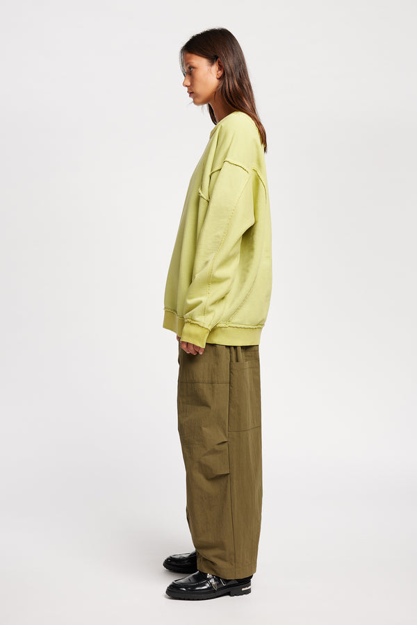 women -side of model wearing Unisex format oversized crew neck sweater in chartreuse with clean panelled design and raw flat-locked seams, displayed from the front.